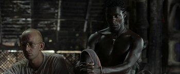 Movie still from “The Beach” (2000), directed by Danny Boyle – A man sitting on the ground with his foot on the ground; Close Up shot, Over the shoulder angle