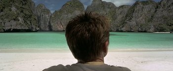 Movie still from “The Beach” (2000), directed by Danny Boyle – A man sitting on the beach looking out at the water; Wide shot, High angle