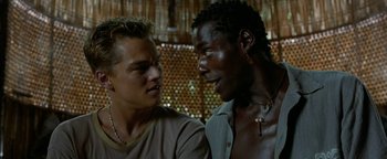 Movie still from “The Beach” (2000), directed by Danny Boyle – Two men talking to each other in front of a wooden wall; Close Up shot, Low angle