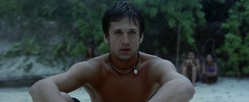 Movie still from “The Beach” (2000), directed by Danny Boyle – A shirtless man sitting in the water with a necklace on; Close Up shot, Low angle