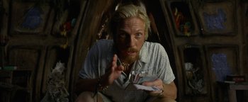 Movie still from “The Beach” (2000), directed by Danny Boyle – A man sitting on the ground holding a phone; Close Up shot, High angle