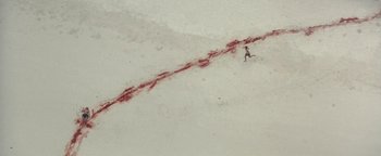 Movie still from “The Beach” (2000), directed by Danny Boyle – A person is walking in the snow near a trail of blood; Extreme Wide shot, Overhead angle