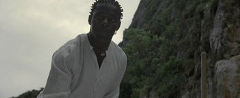 Movie still from “The Beach” (2000), directed by Danny Boyle – A man in a white shirt is standing in front of a mountain; Close Up shot, Low angle