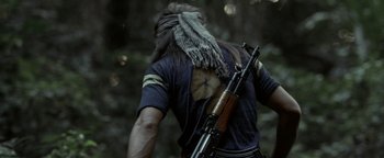 Movie still from “The Beach” (2000), directed by Danny Boyle – A man with a long hair and a beard is holding a rifle; Medium shot, Over the shoulder angle