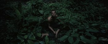 Movie still from “The Beach” (2000), directed by Danny Boyle – A man sitting on the ground surrounded by green plants; Wide shot, Overhead angle