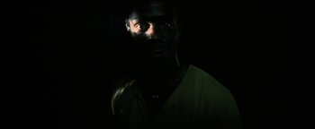 Movie still from “The Beach” (2000), directed by Danny Boyle – A man in a green shirt is in the dark; Close Up shot, High angle