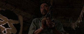Movie still from “The Beach” (2000), directed by Danny Boyle – A man holding a gun up to his face; Medium shot, Low angle