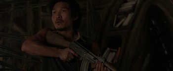 Movie still from “The Beach” (2000), directed by Danny Boyle – A man holding an ak - 4 7 rifle in his hand; Medium shot, Over the shoulder angle