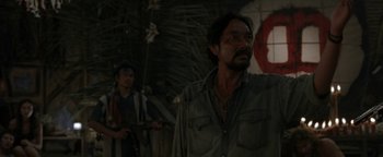 Movie still from “The Beach” (2000), directed by Danny Boyle – A man standing next to another man in front of a tree; Medium shot, Over the shoulder angle