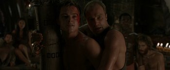 Movie still from “The Beach” (2000), directed by Danny Boyle – Two shirtless men standing next to each other in a dark room; Medium shot, Low angle