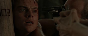 Movie still from “The Beach” (2000), directed by Danny Boyle – A man is holding a gun while looking at another man; Close Up shot, Over the shoulder angle