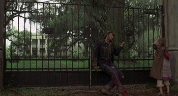 Movie still from “The Beguiled” (1971), directed by Don Siegel – A man sitting on the ground next to an iron gate; Wide shot, Low angle