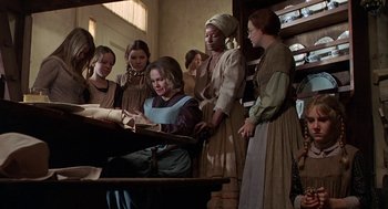 Movie still from “The Beguiled” (1971), directed by Don Siegel – A group of women standing around a table with a book; Medium shot, High angle