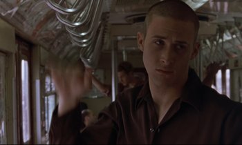 Movie still from “The Believer” (2001), directed by Henry Bean – A man in brown shirt standing on a train; Close Up shot, Low angle