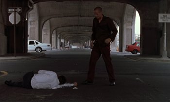 Movie still from “The Believer” (2001), directed by Henry Bean – A man standing next to another man laying on the ground; Wide shot, Low angle