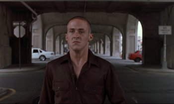 Movie still from “The Believer” (2001), directed by Henry Bean – A man in a brown shirt standing under an overpass; Medium shot, Low angle