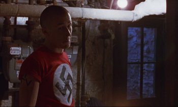 Movie still from “The Believer” (2001), directed by Henry Bean – A man in a red shirt is standing in a room; Medium shot, High angle