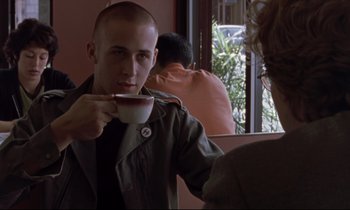 Movie still from “The Believer” (2001), directed by Henry Bean – A man holding a cup of coffee in a room; Medium shot, Over the shoulder angle