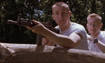 Movie still from “The Believer” (2001), directed by Henry Bean – A man holding an ak - 4 7 rifle while standing next to a tree; Close Up shot, Low angle