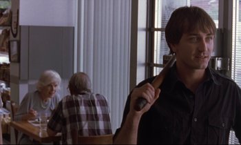 Movie still from “The Believer” (2001), directed by Henry Bean – A man holding a baseball bat in front of a group of people; Medium shot, Over the shoulder angle