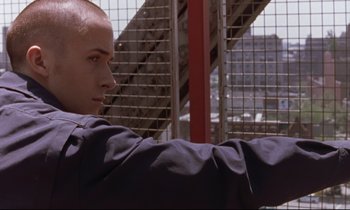 Movie still from “The Believer” (2001), directed by Henry Bean – A man sitting in front of a metal fence; Close Up shot, Low angle