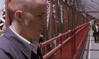 Movie still from “The Believer” (2001), directed by Henry Bean – A man in a suit and tie standing next to a red fence; Close Up shot, Over the shoulder angle