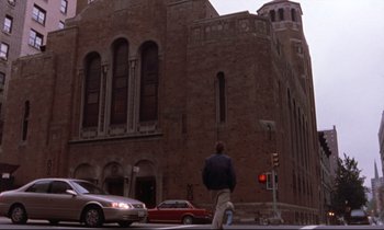 Movie still from “The Believer” (2001), directed by Henry Bean – A man walking across the street in front of a building; Extreme Wide shot, Low angle