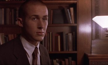 Movie still from “The Believer” (2001), directed by Henry Bean – A man in a suit and tie in front of a bookshelf; Close Up shot, Low angle