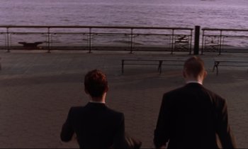 Movie still from “The Believer” (2001), directed by Henry Bean – Two men in suits sitting on a bench near the water; Wide shot, High angle