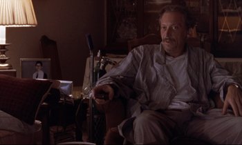 Movie still from “The Believer” (2001), directed by Henry Bean – A man sitting in a chair holding a remote control; Medium shot, Low angle
