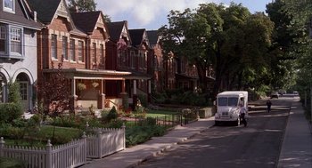 Movie still from “The Believers” (1987), directed by John Schlesinger – A white bus driving down a street past a row of houses; Extreme Wide shot, High angle