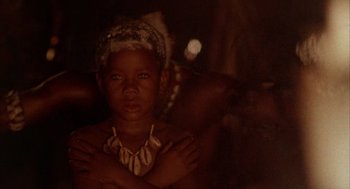Movie still from “The Believers” (1987), directed by John Schlesinger – A young girl wearing a necklace in a dark room; Close Up shot, High angle