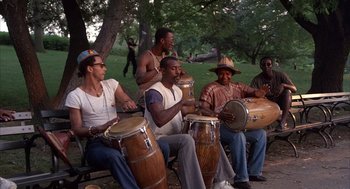 Movie still from “The Believers” (1987), directed by John Schlesinger – A group of men sitting on top of a wooden bench; Wide shot, Low angle
