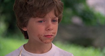 Movie still from “The Believers” (1987), directed by John Schlesinger – A young boy with brown powder all over his face; Close Up shot, Over the shoulder angle