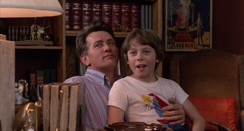 Movie still from “The Believers” (1987), directed by John Schlesinger – A man and a boy sitting next to each other in a room; Medium shot, Low angle