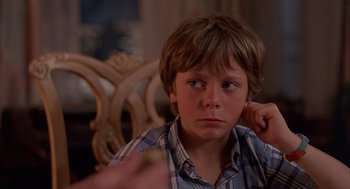 Movie still from “The Believers” (1987), directed by John Schlesinger – A young boy sitting in a chair with his hand on his ear; Close Up shot, Over the shoulder angle