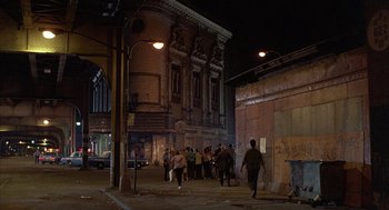Movie still from “The Believers” (1987), directed by John Schlesinger – A group of people walking down a street at night; Extreme Wide shot, High angle