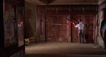 Movie still from “The Believers” (1987), directed by John Schlesinger – A man holding a sword in an empty room; Wide shot, High angle