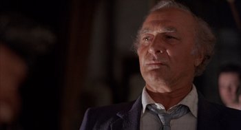 Movie still from “The Believers” (1987), directed by John Schlesinger – An older man wearing a suit and tie looking at the camera; Close Up shot, Low angle