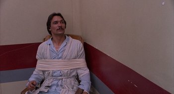 Movie still from “The Believers” (1987), directed by John Schlesinger – A man in a bathrobe is tied to a wall; Medium shot, High angle