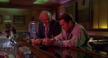 Movie still from “The Believers” (1987), directed by John Schlesinger – Two men sitting at a bar looking at a cell phone; Medium shot, Low angle