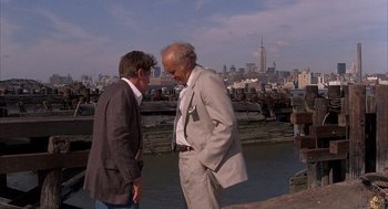 Movie still from “The Believers” (1987), directed by John Schlesinger – Two older men standing next to each other near a body of water; Wide shot, Over the shoulder angle