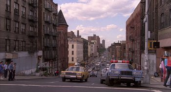Movie still from “The Believers” (1987), directed by John Schlesinger – A city street filled with lots of traffic and parked cars; Extreme Wide shot, Low angle