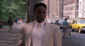 Movie still from “The Believers” (1987), directed by John Schlesinger – A man wearing a suit and tie standing on the sidewalk; Close Up shot, Low angle