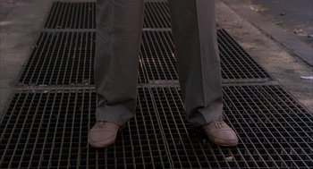 Movie still from “The Believers” (1987), directed by John Schlesinger – A man in dress shoes standing on a grate; Medium shot, High angle