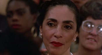 Movie still from “The Believers” (1987), directed by John Schlesinger – An older woman wearing a pearl necklace and red lipstick; Close Up shot, Over the shoulder angle
