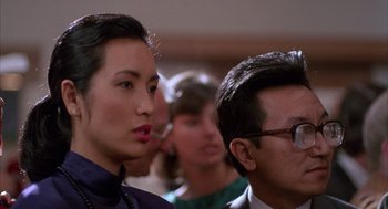 Movie still from “The Believers” (1987), directed by John Schlesinger – A man and a woman standing next to each other in front of other people; Close Up shot, Over the shoulder angle