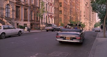 Movie still from “The Believers” (1987), directed by John Schlesinger – A car driving down a street past tall buildings; Extreme Wide shot, High angle