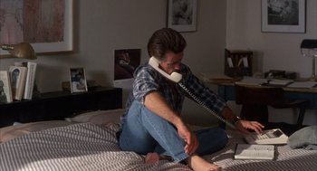 Movie still from “The Believers” (1987), directed by John Schlesinger – A man sitting on a bed talking on a phone; Medium shot, High angle