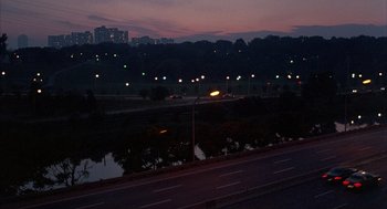 Movie still from “The Believers” (1987), directed by John Schlesinger – A view of a city at night from a bridge; Extreme Wide shot, High angle